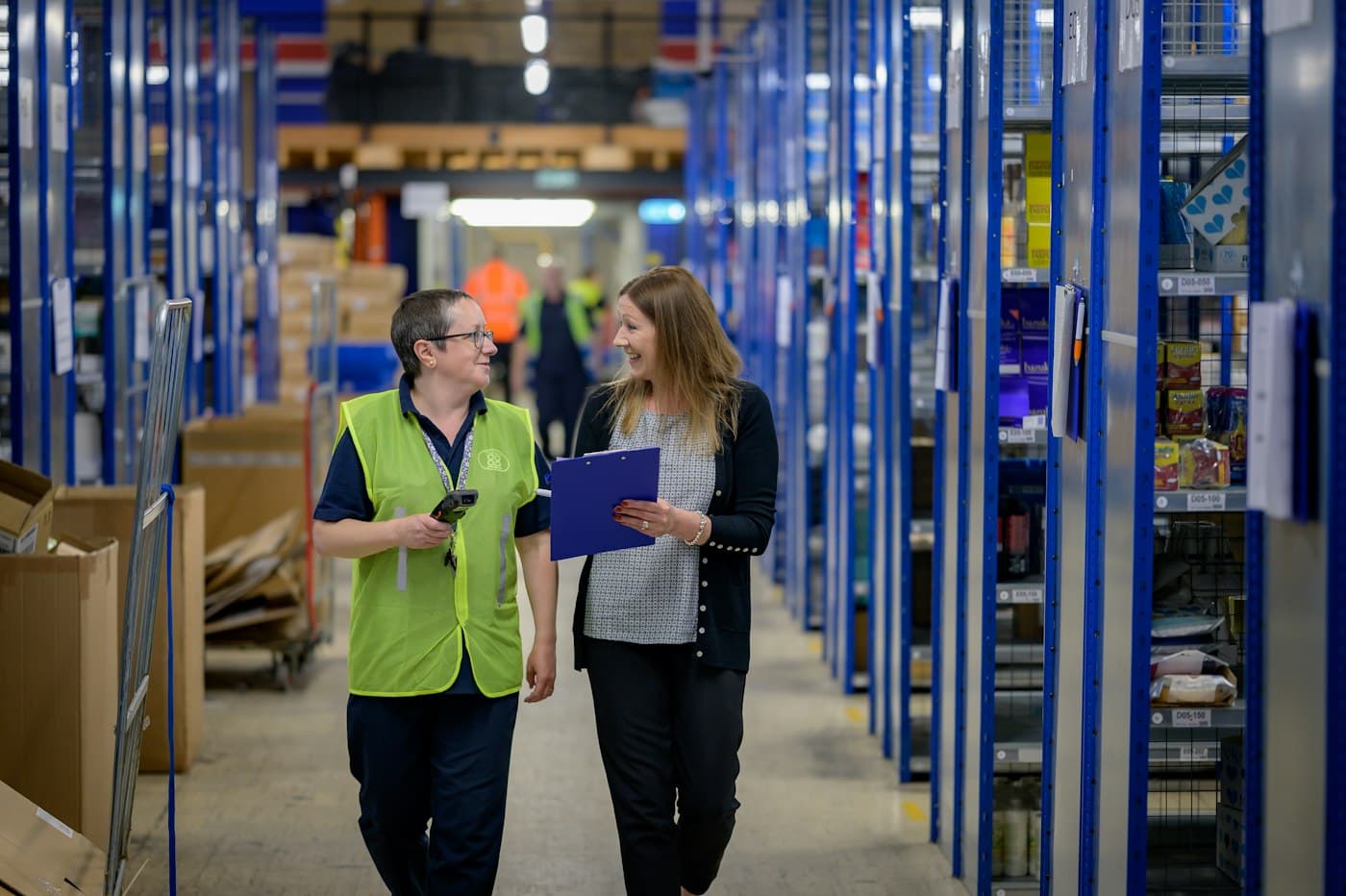 Two warehouse colleagues walking an aisle between blue shelving racks