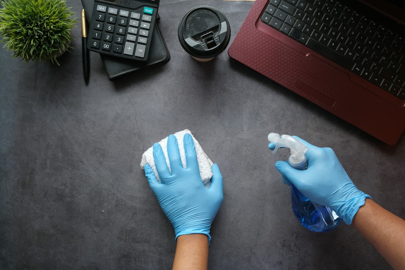 Gloved hands wiping down a desk with spray and a cloth